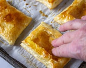 Finger tips pushing down the center of a puff pastry shell.