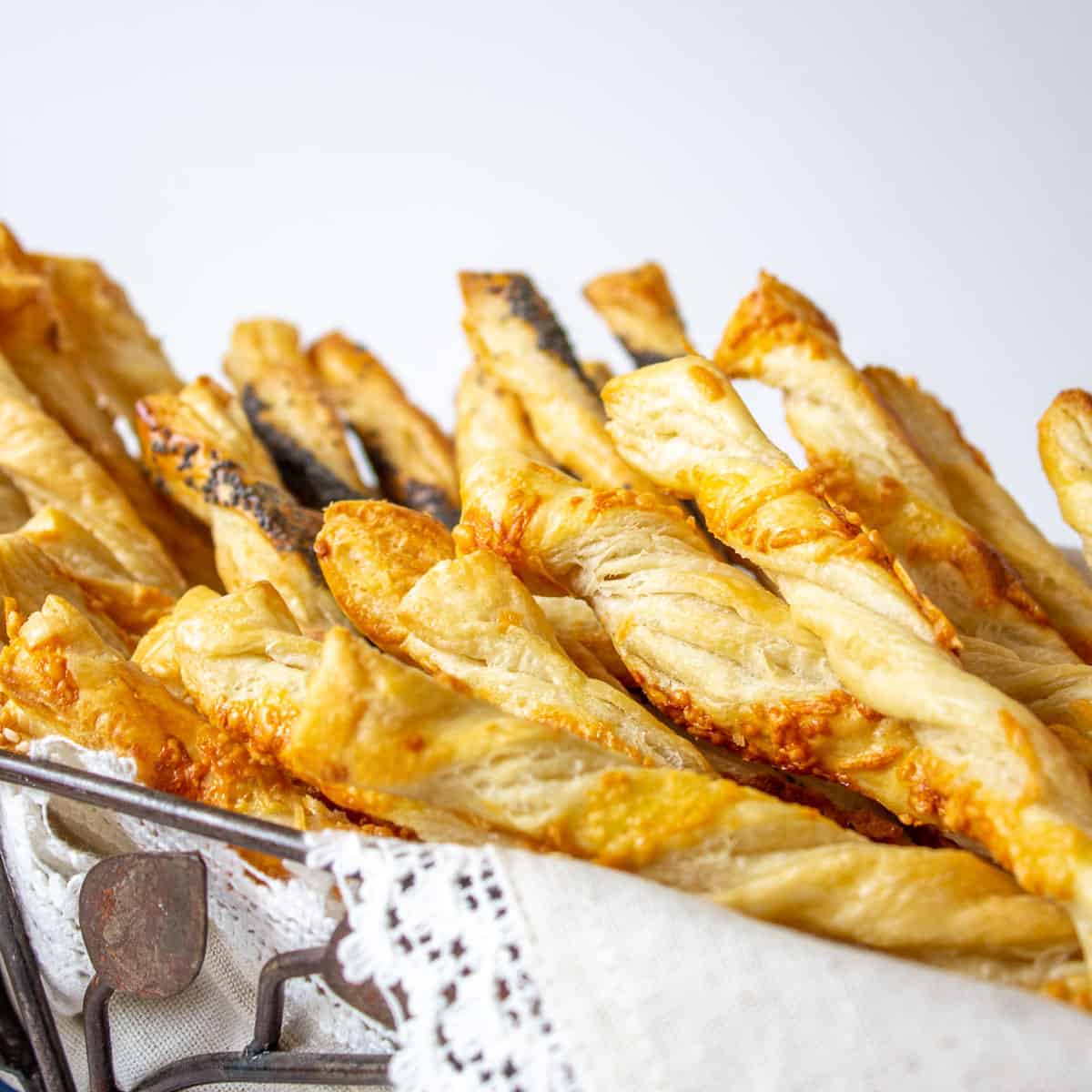 Puff pastry twists topped with sesame seeds in a metal basket. 