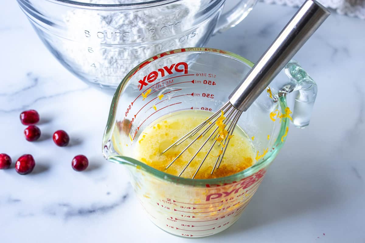 A glass measuring cup with a whisk and yellow liquid.