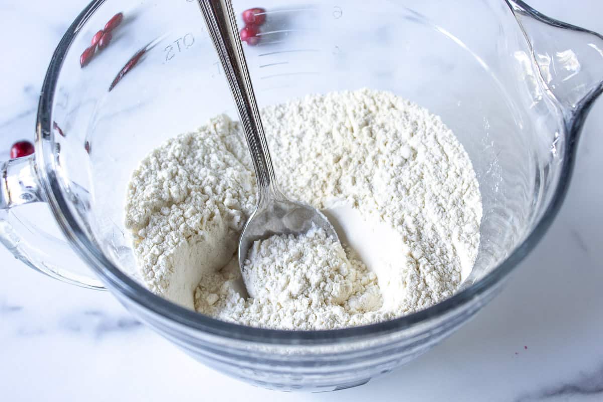 Flour in a glass bowl with a spoon.