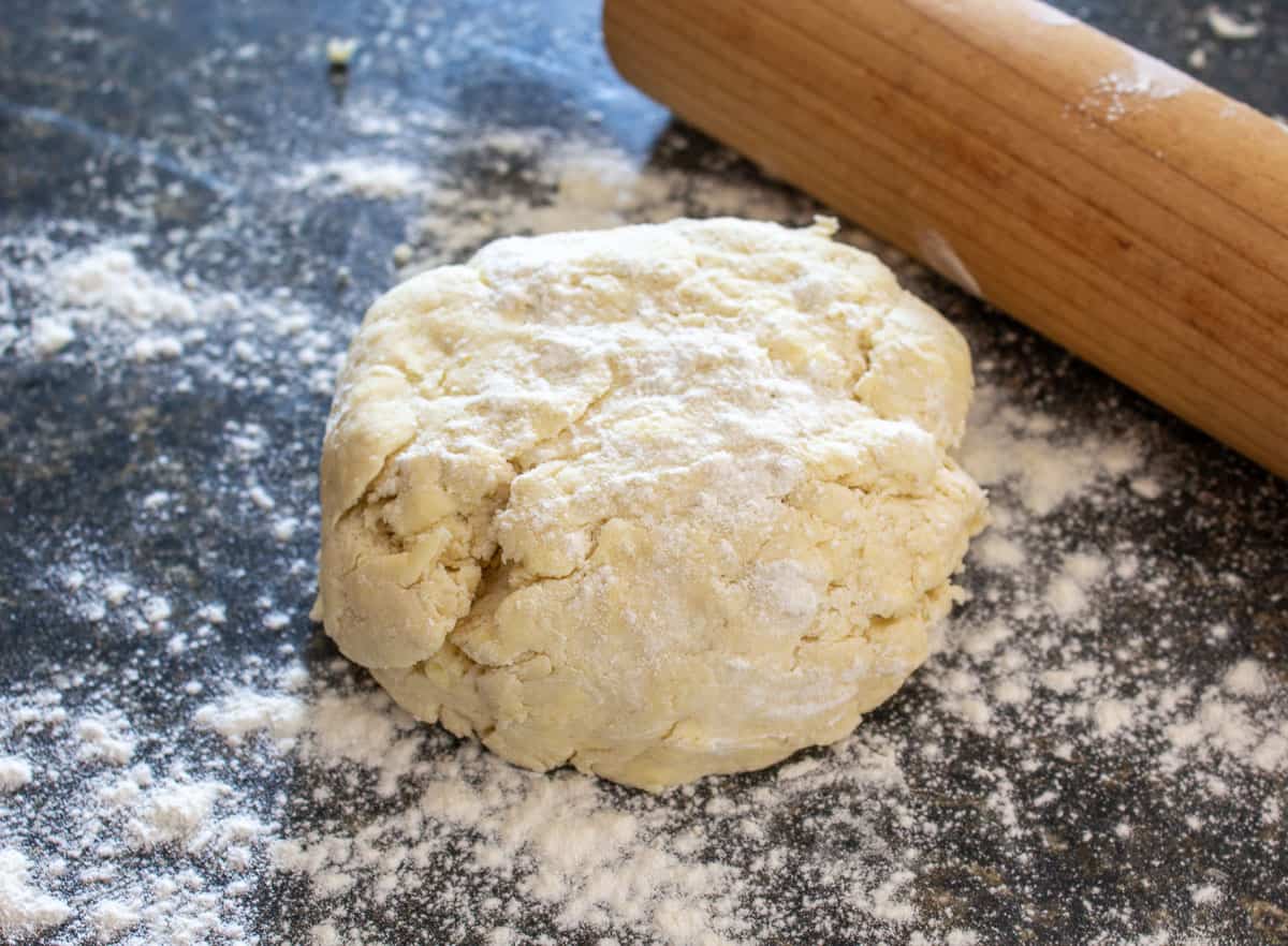 Puff pastry dough on a floured surface with a wooden rolling pin next to the dough.