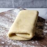 Folded puff pastry on a floured wooden board.