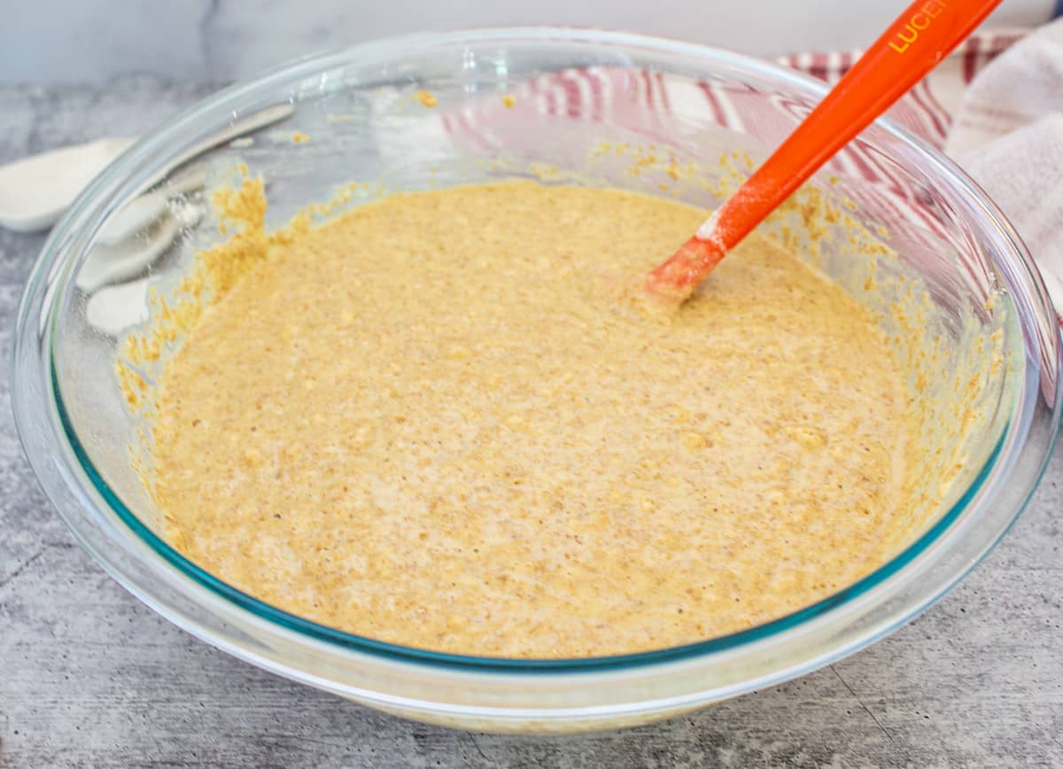 Mixed muffin batter in a glass bowl with an orange spatula in batter.