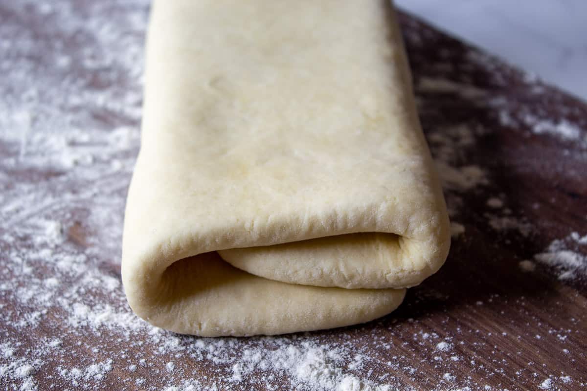 Rolled and folded rough puff pastry dough on a floured surface.