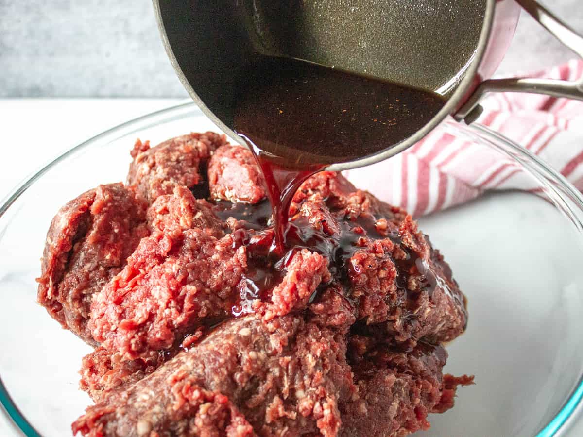 Pouring liquid marinade over the top of ground burger.