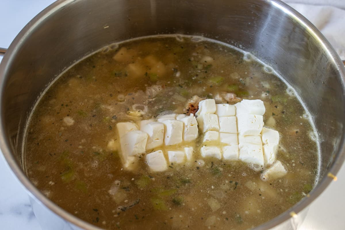 Cream cheese cubes in a pot filled with chicken broth.