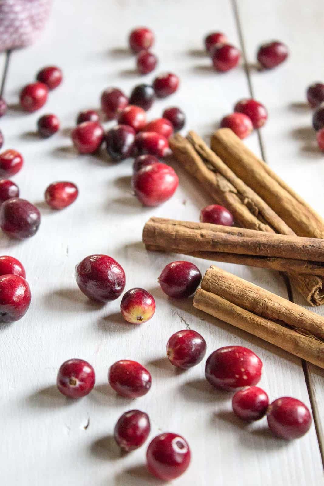 Fresh cranberries and cinnamon sticks scattered on a white board.