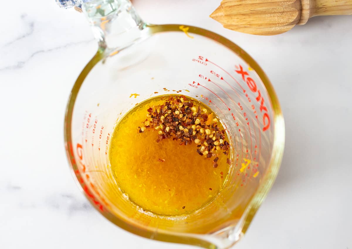 A glass measuring cup filled with an orange vinaigrette and red pepper flakes. 