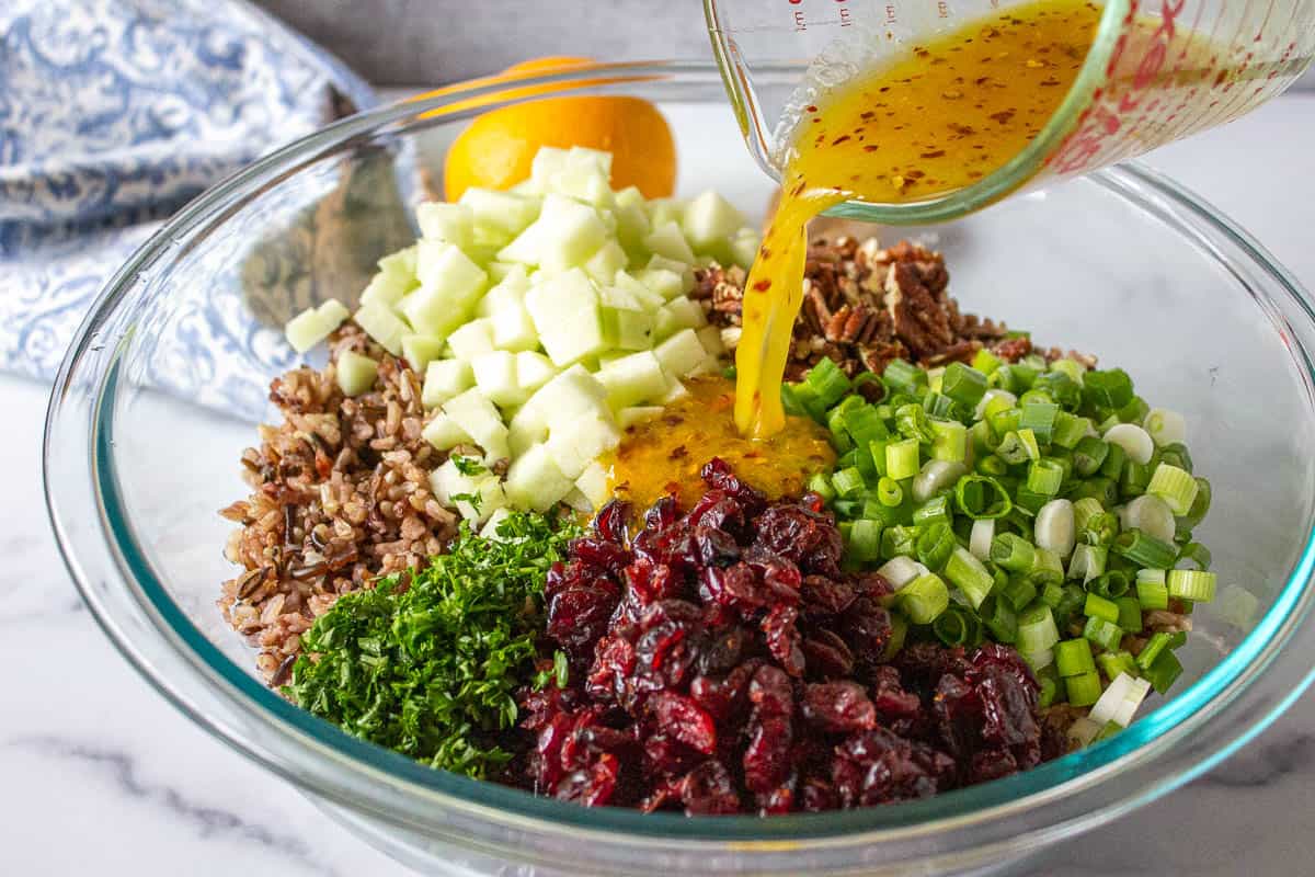 An orange vinaigrette being poured over a bowl filled with rice salad.