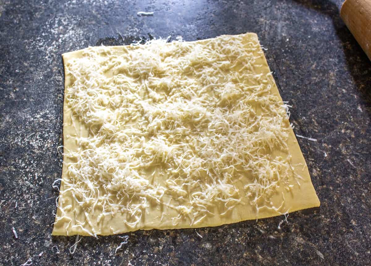 Shredded parmesan cheese sprinkled on top of a square of dough.