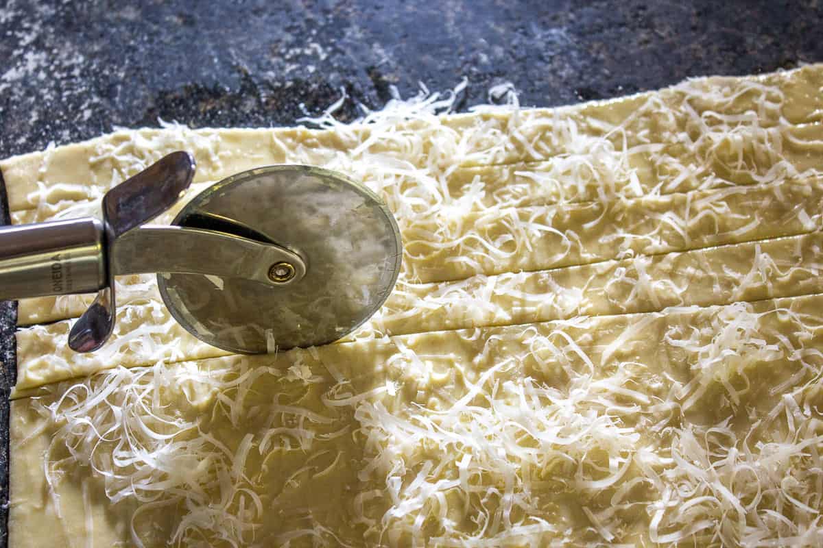 A pizza cutter slicing strips of dough.