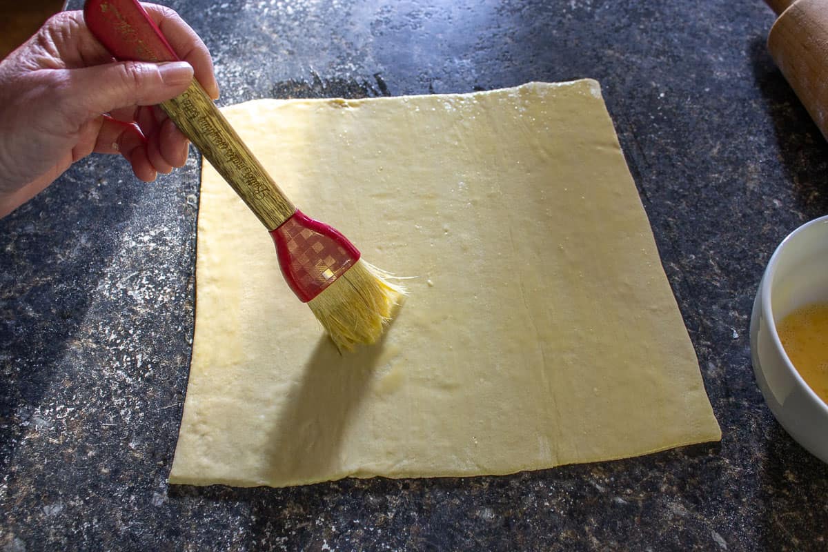 Puff pastry dough being brushed with an egg wash. 