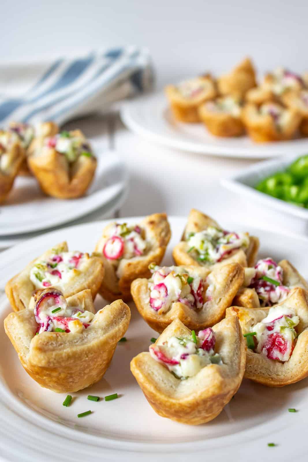 A white plate filled with bite sized puff pastry shells filled with a cream cheese mixture.