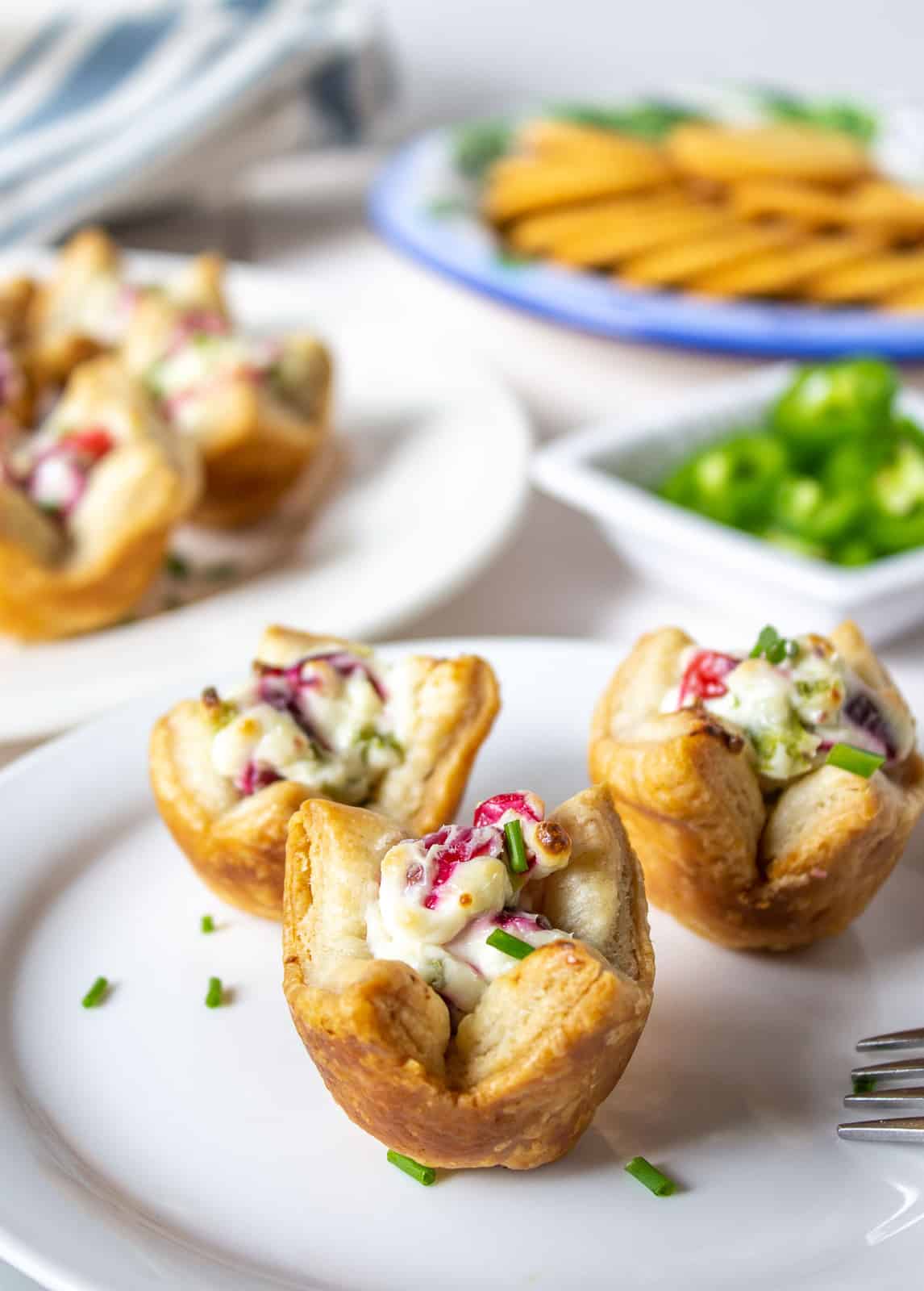 Three puff pastry cups filled with cranberries and cream cheese on a white plate.