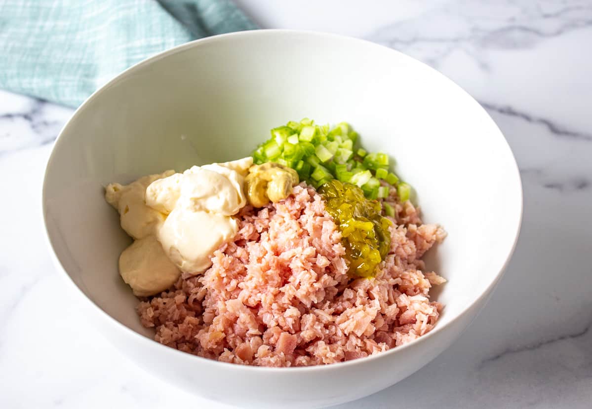 A white bowl filled with chopped ham, diced celery and mayonnaise.