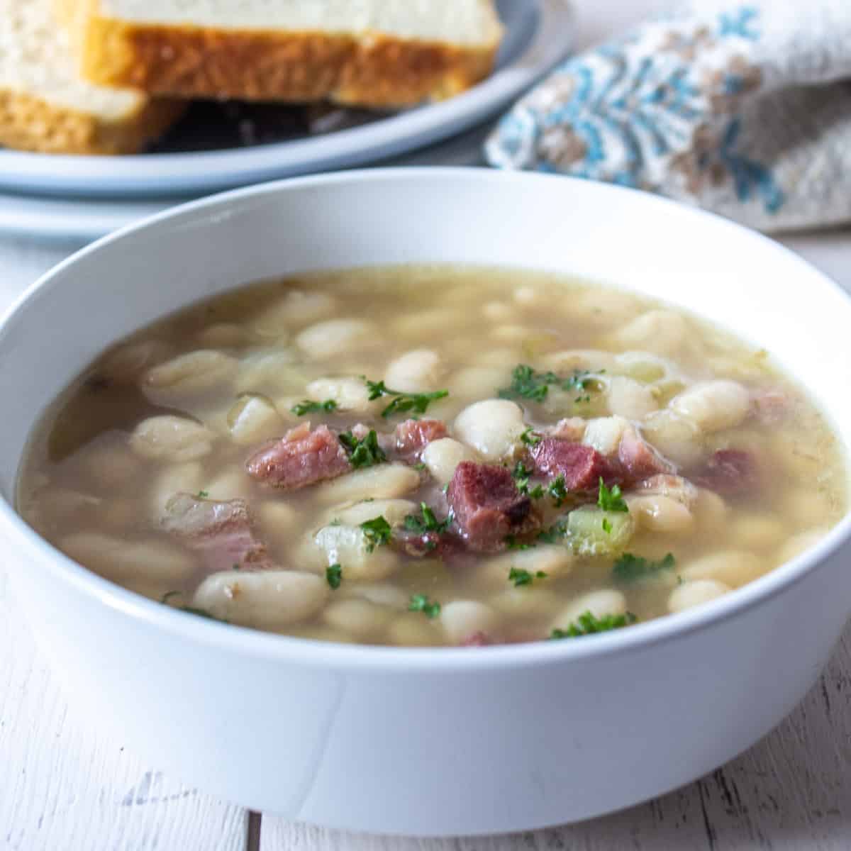 A white bowl filled with soup with beans and ham.