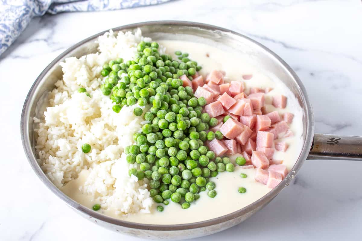 A white sauce with rice, peas and ham in a pan.