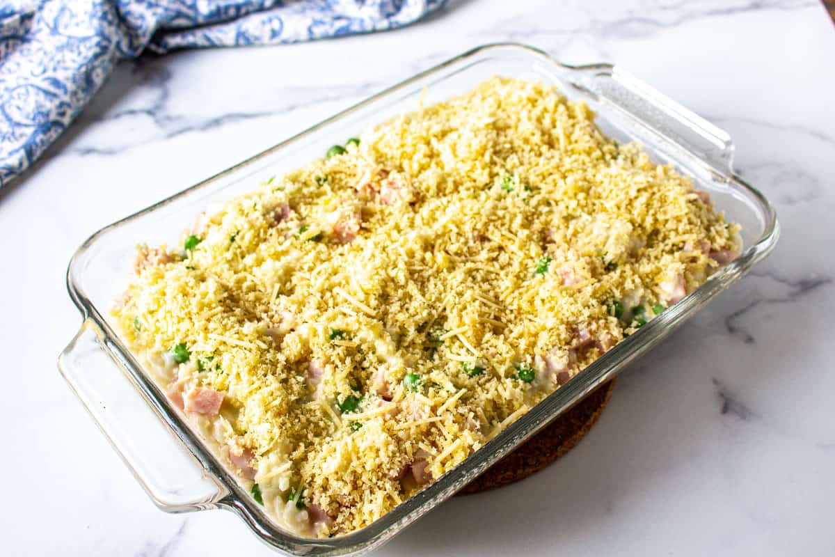 An unbaked casserole topped with panko bread crumbs in a glass baking dish.