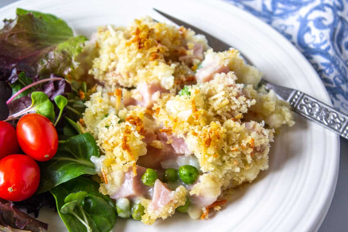 A rice casserole with ham and peas on a white plate.