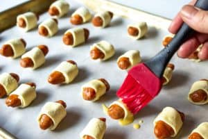 A red pastry brush adding an egg wash to little smokies wrapped in puff pastry.