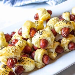 Mini pigs in a blanket piled onto a white platter.