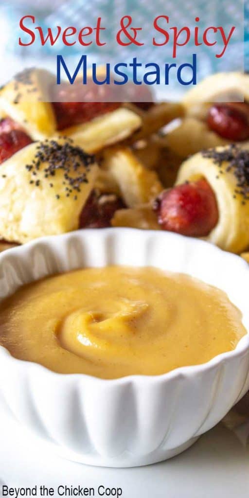 A white dish filled with a golden mustard with small sausages behind the mustard.