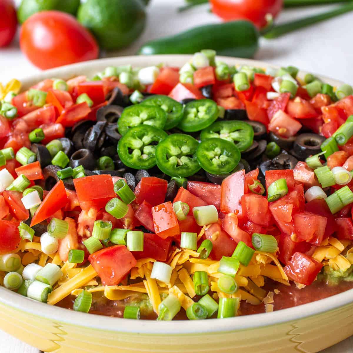 A layered dip topped with chopped tomatoes, olives and sliced jalapenos.