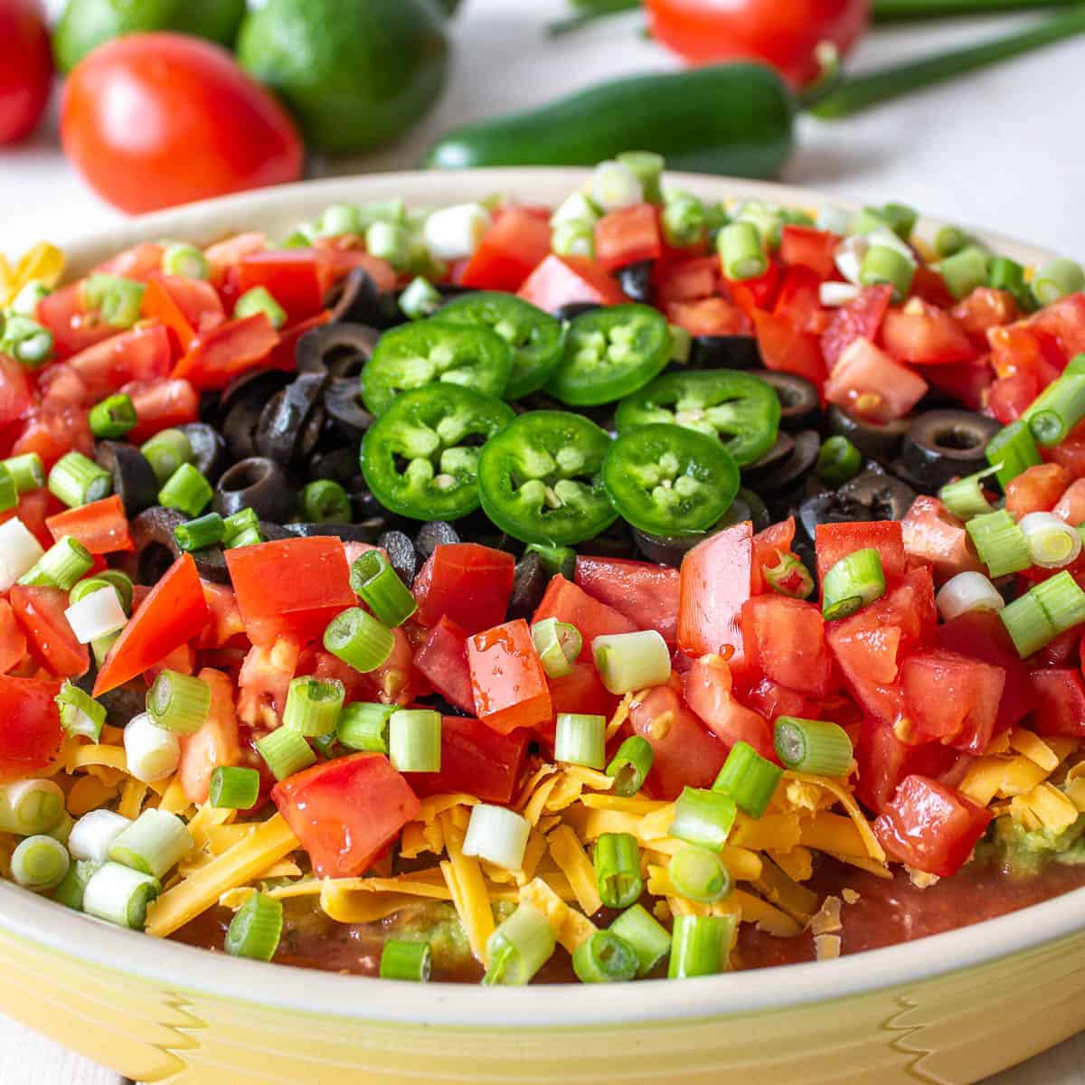 Mexican layered dip topped with chopped tomatoes, olives and sliced jalapenos.