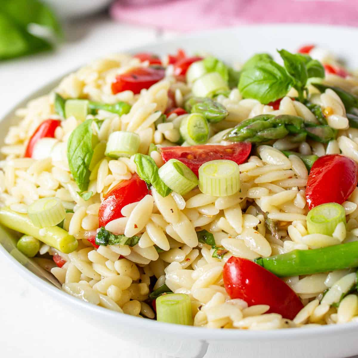 Orzo pasta with asparagus and tomatoes in a white bowl.