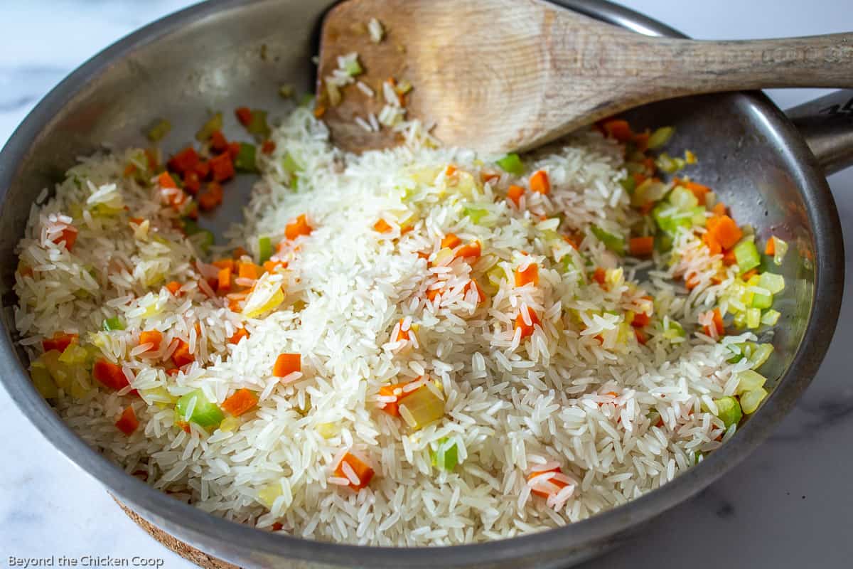 A sauté pan filled with rice, carrots and onions.  