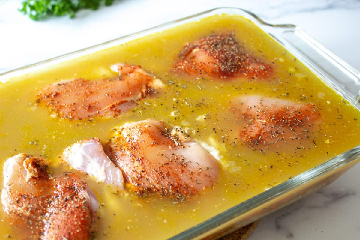 A casserole dish filled with chicken broth and skinless chicken thighs.