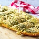 Sliced cheesy pesto bread on a wooden board.