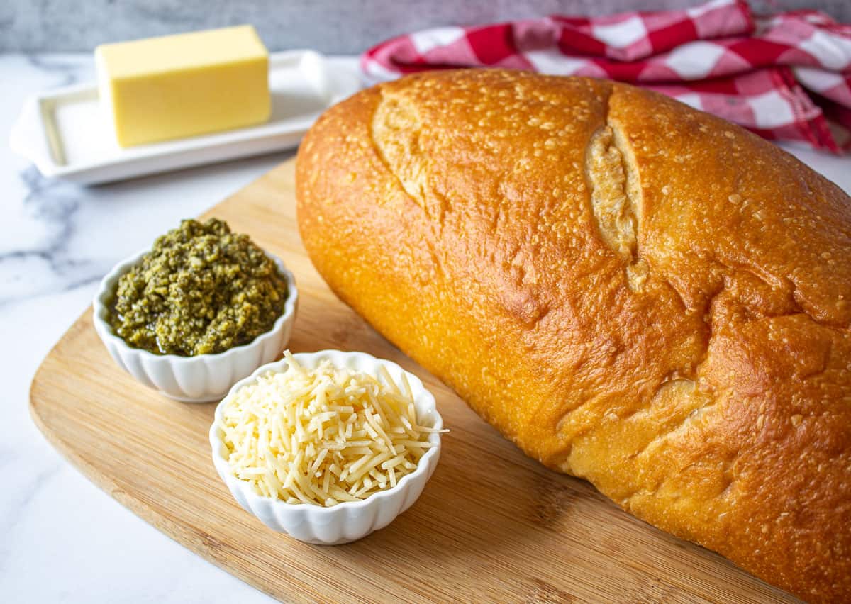 A loaf of french bread next to two small bowls filled with pesto and parmesan cheese.