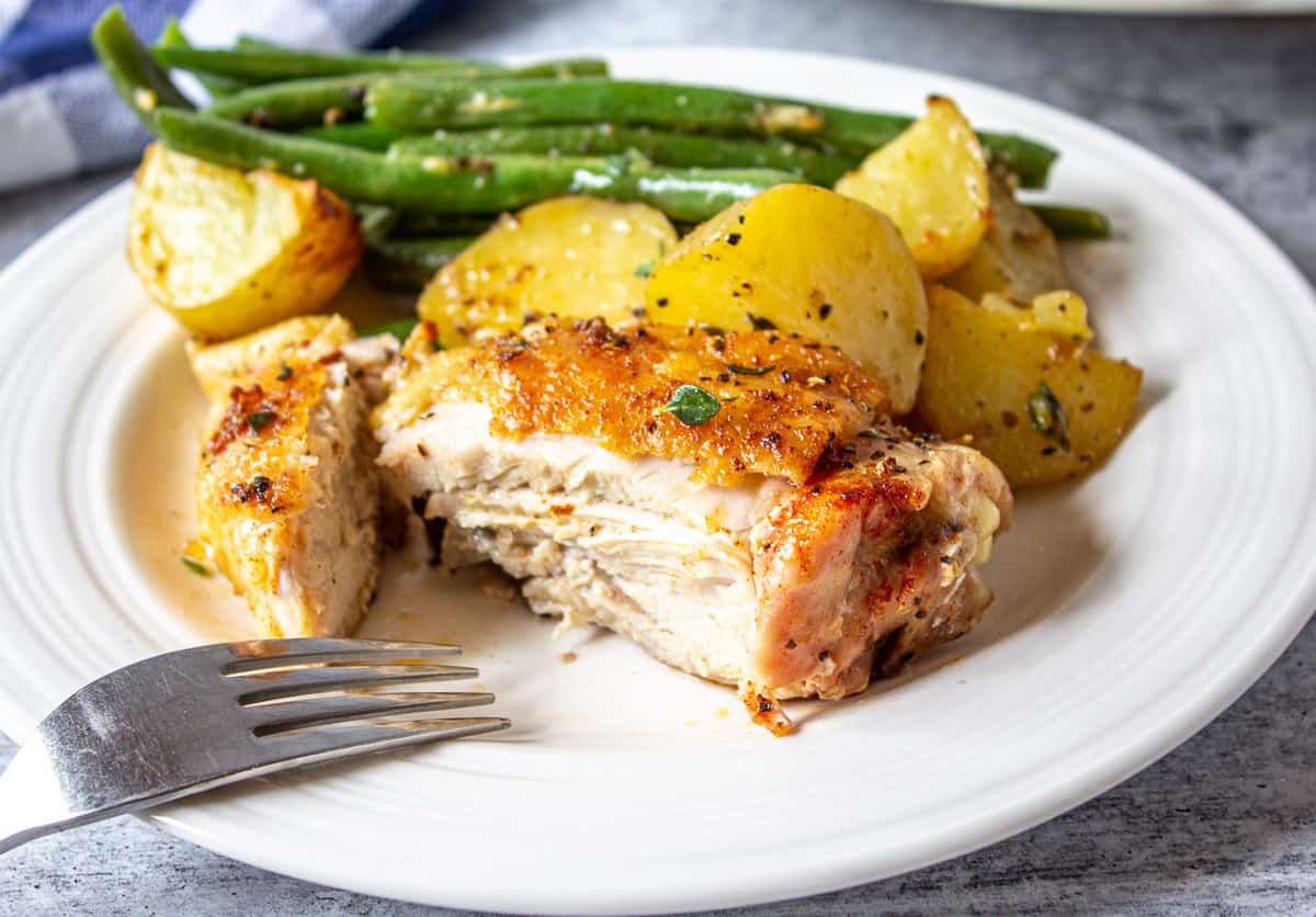 Cut chicken thigh on a plate with potatoes and green beans.