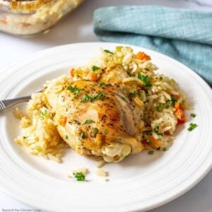 Rice pilaf topped with a cooked chicken thigh on a white plate.