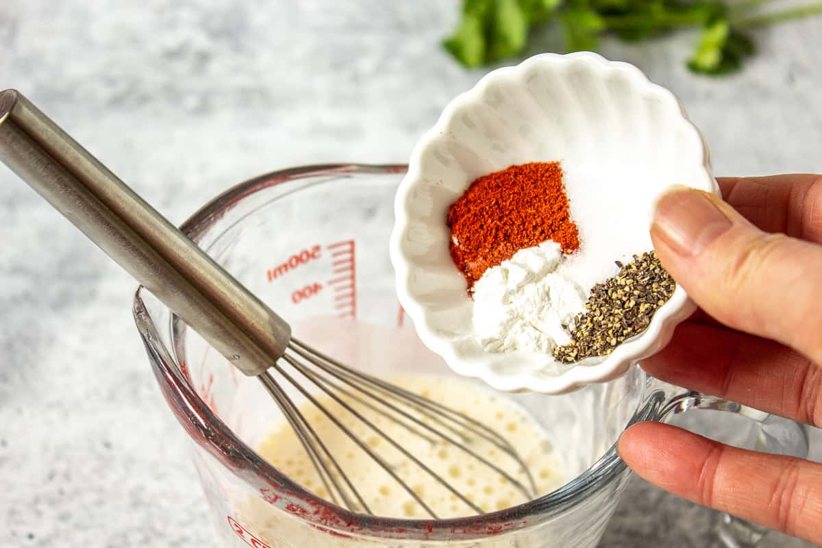 A small bowl filled with seasonings being added to a glass measuring cup with milk. 