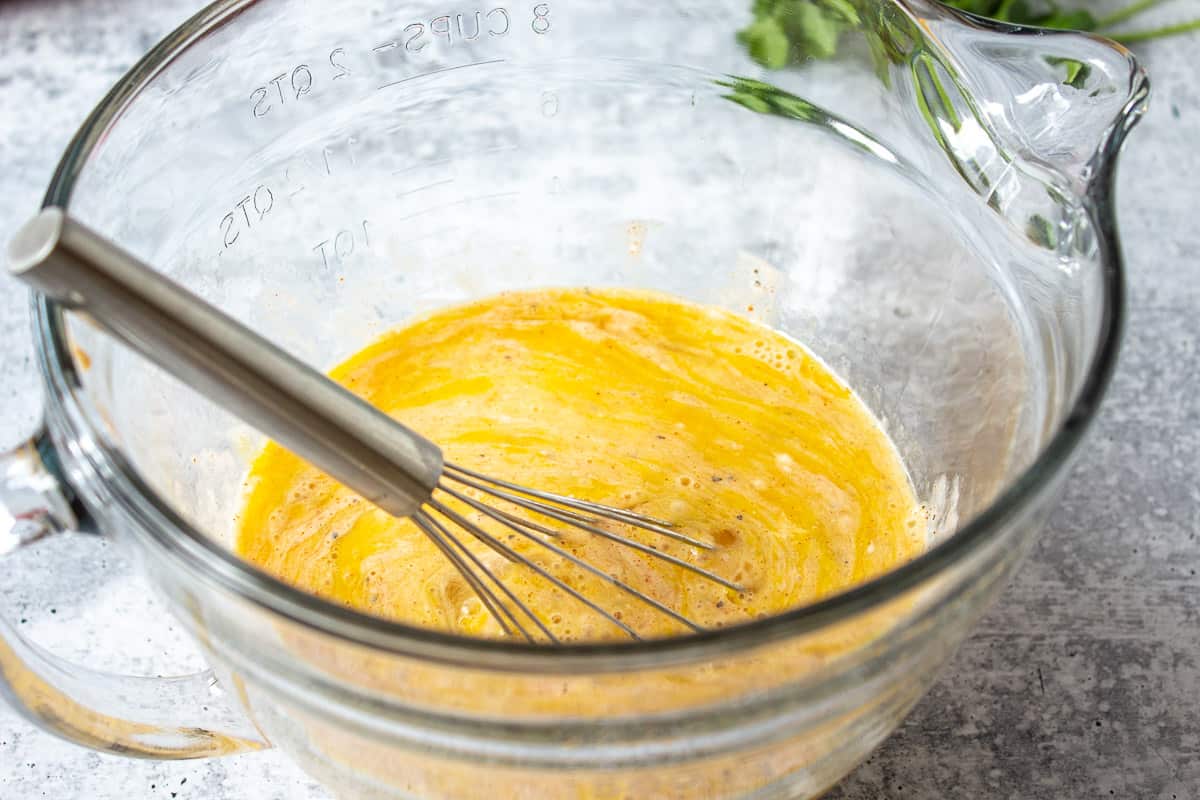 An egg mixture in a glass bowl with a whisk.