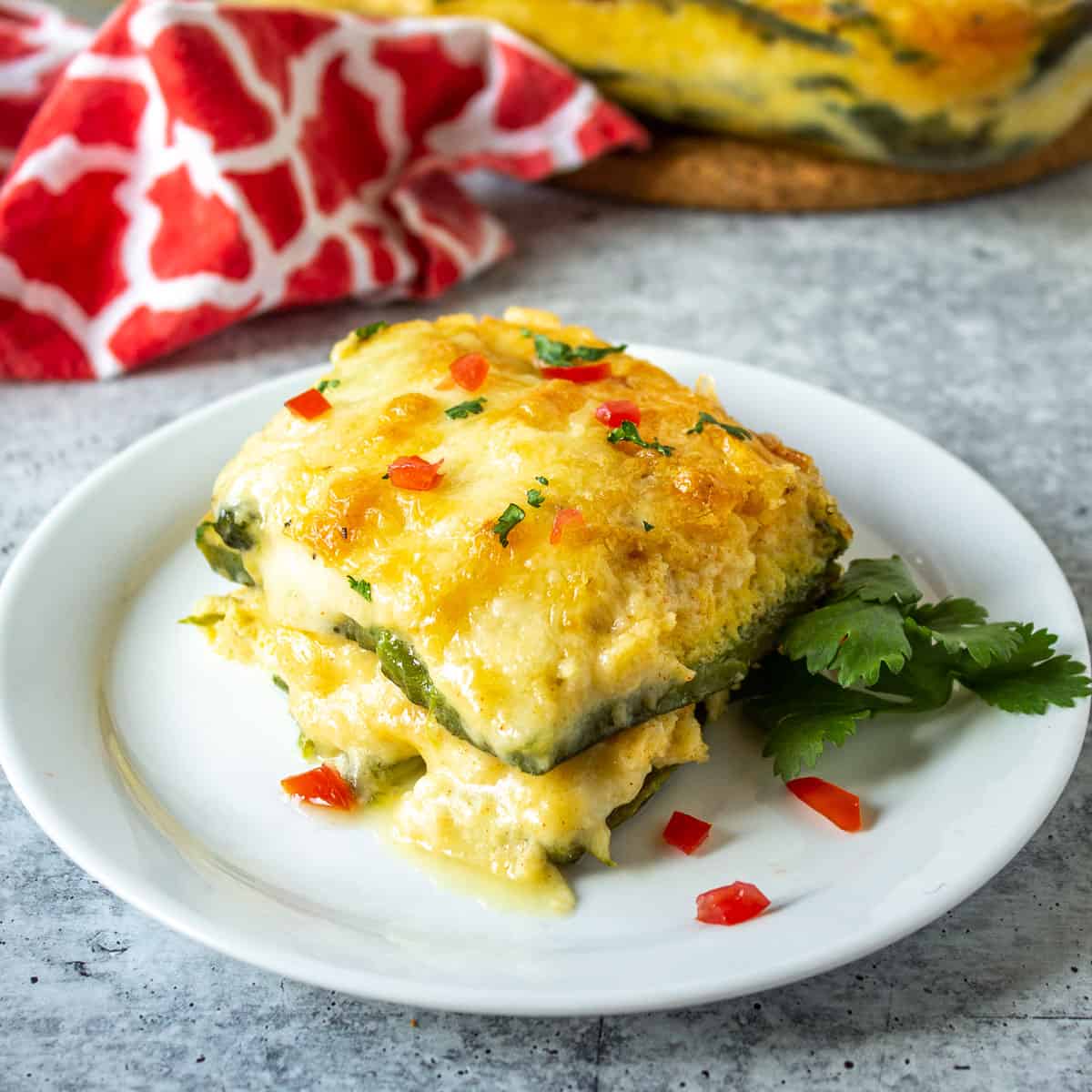 A slice of chile relleno casserole topped with finely diced tomatoes and fresh cilantro.