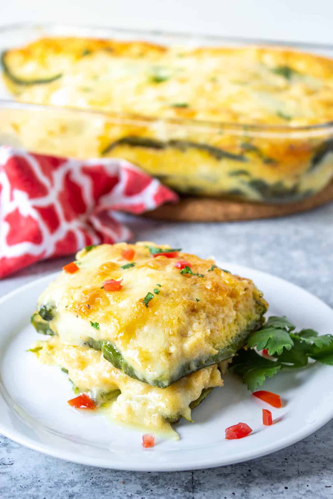 A slice of chile relleno casserole on a white plate with the entire casserole in the background.