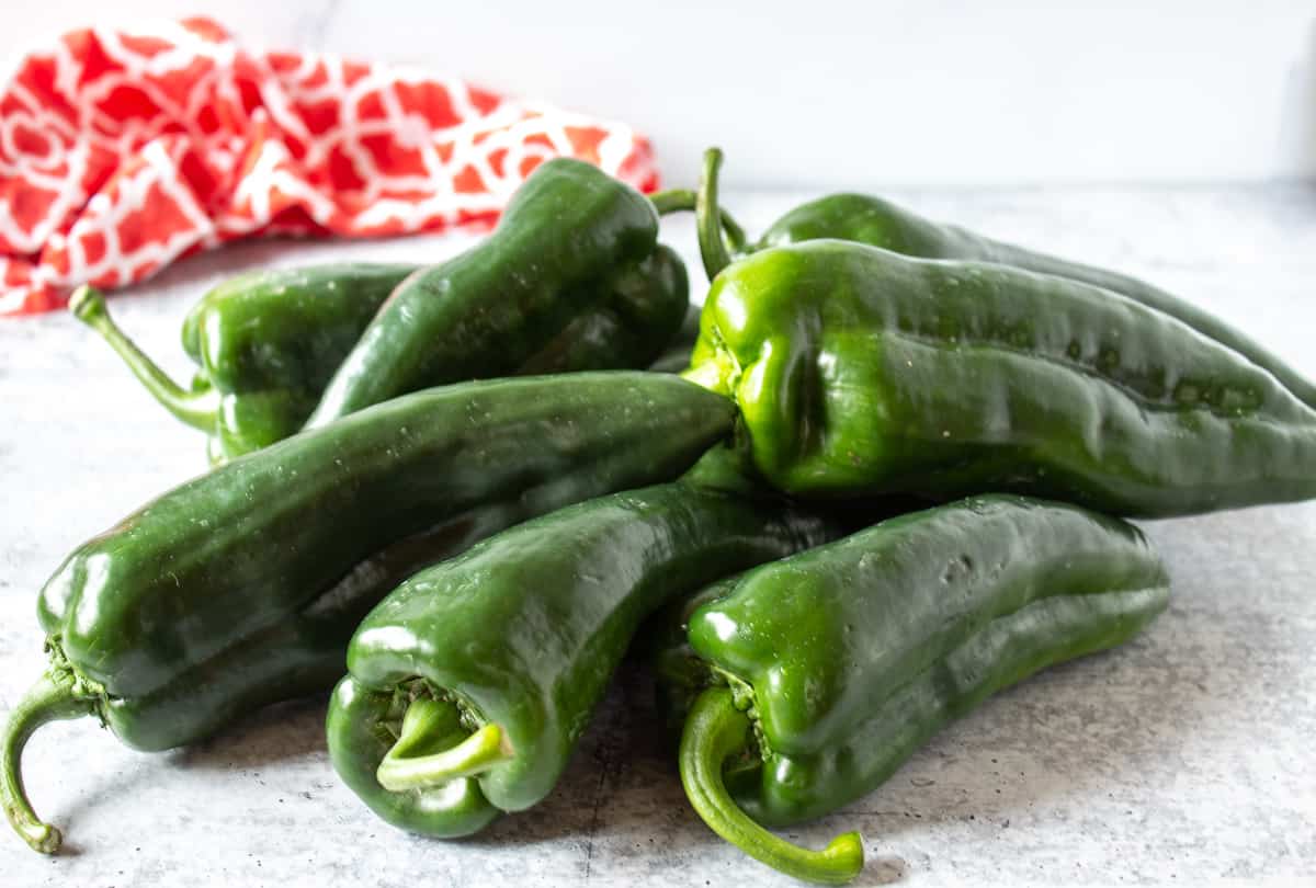 Poblano peppers piled in a stack  on a countertop.