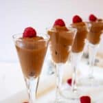 Small glass filled with chocolate mousse and topped with a reapberry.