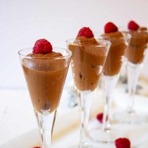 Small glass filled with chocolate mousse and topped with a reapberry.