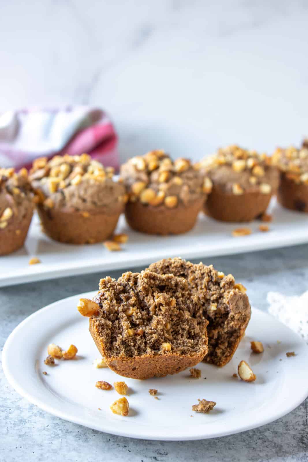 A chocolate muffin filled with chocolate chips and topped with chopped peanuts on a white plate.