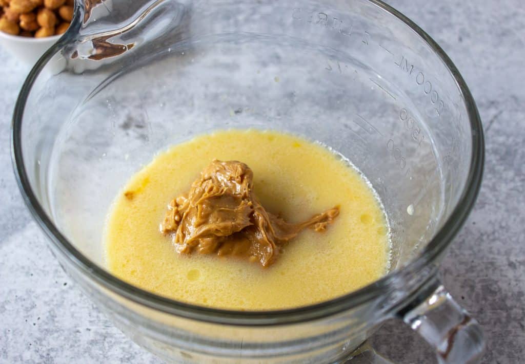 Peanut butter sitting in the middle of yellow liquid ingredients in a glass bowl.