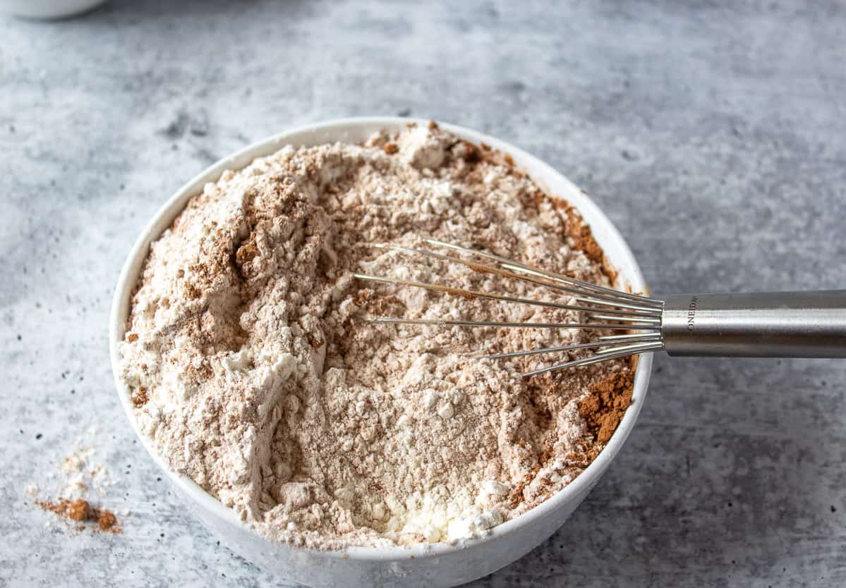 A white bowl filled with flour and cocoa powder with a wire whisk in the bowl.