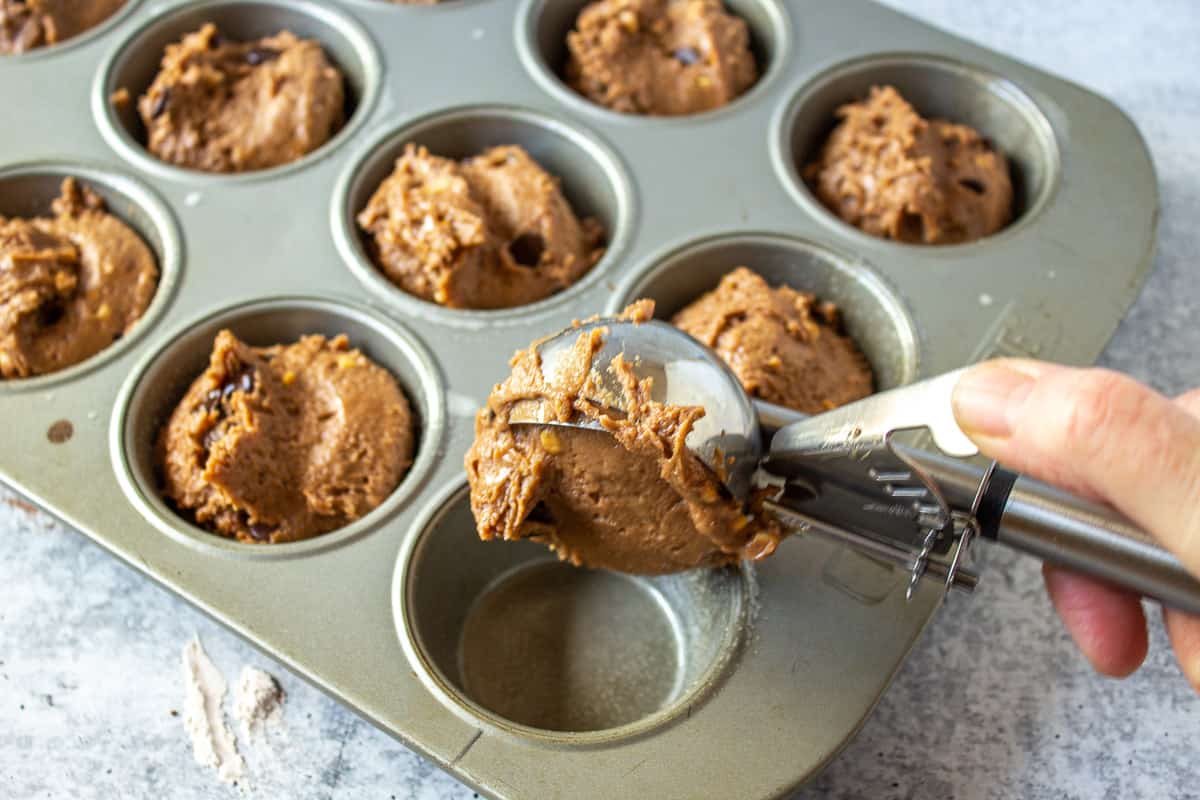 Scooping chocolate peanut butter muffin batter into muffin tins.