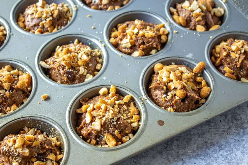 Chopped peanuts sprinkled on top of chocolate muffins in a muffin tin.