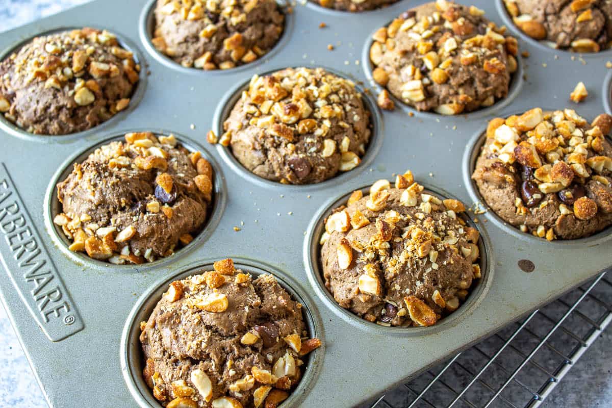 Cooked chocolate muffins topped with peanuts in a muffin tin.