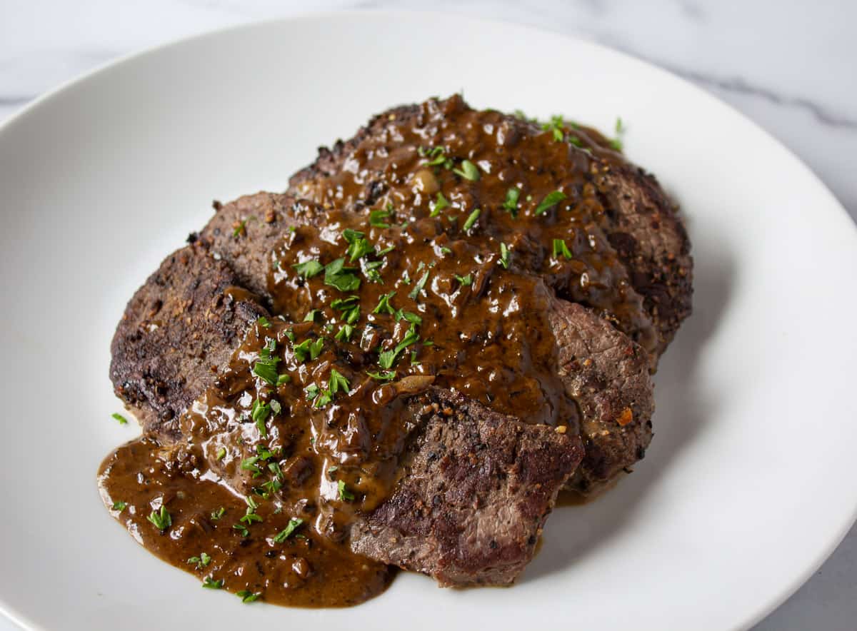 Elk steaks topped with a brown sauce and parsley.