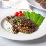 Elk steak topped with a brown sauce and freshly chopped parsley.